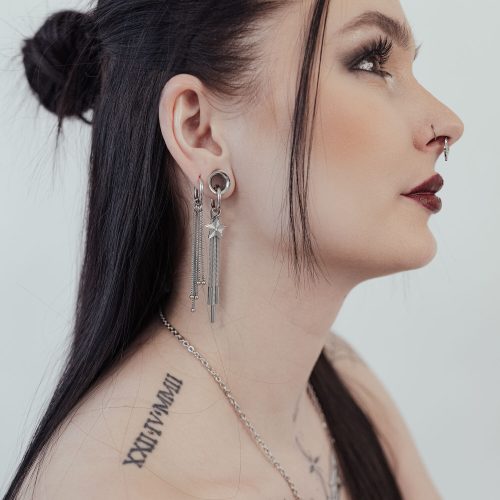 Frau mit langen schwarzen Haaren trägt silberne Little Shooting Star Hoops und hat Tattoos am Hals.