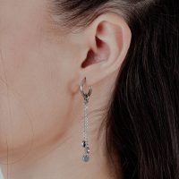 Silberne Creolen mit Kettenanhänger an weiblichem Ohr vor hellem Hintergrund