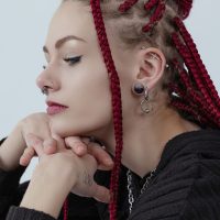 Frau mit roten Dreadlocks trägt silberne Ohrringe und Nasenpiercings, seitliches Profil