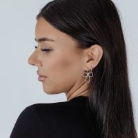 Frau mit silbernen Little Twisted Bow Hoops vor hellem Hintergrund
