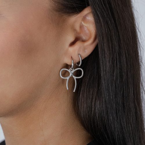 Silberne Little Twisted Bow Hoops getragen am Ohr einer Frau mit dunklem Haar