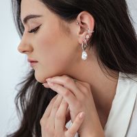 Seitenansicht einer Frau mit Barock-Perlen Creolen und weiteren Ohrringen auf hellem Hintergrund