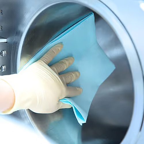 Hand mit Handschuh reinigt Kessel mit blauem Tuch, metallische Oberfläche