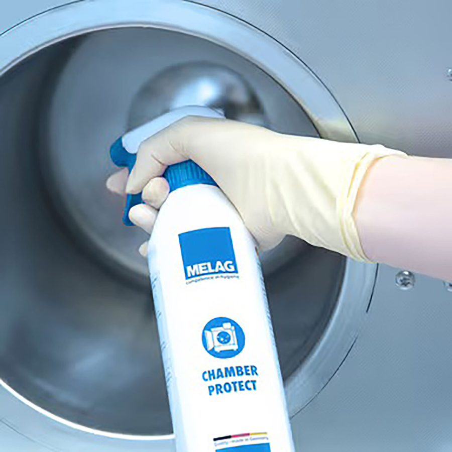 Hand mit gelbem Handschuh hält Sprühflasche Chamber Protect vor rundem Metallkessel