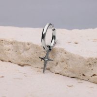 Silberner Ohrring mit polarsternförmigem Anhänger auf hellem Stein