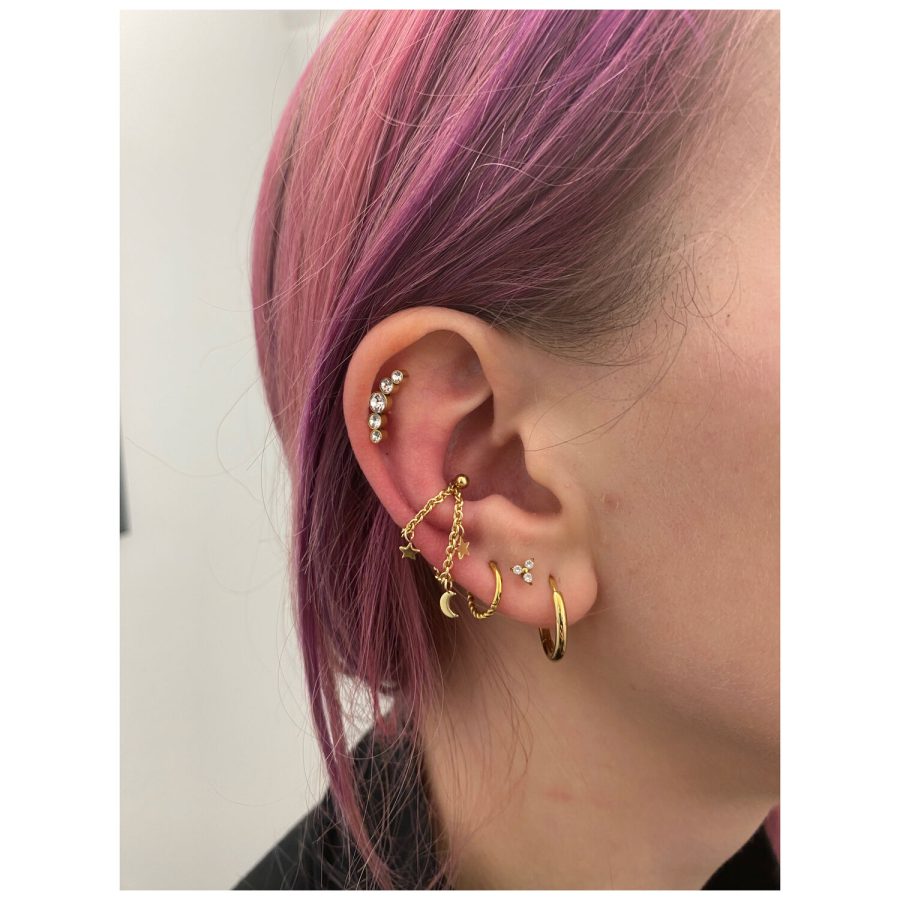 Goldene Piercingkette mit Mond- und Sternmotiven am Ohr getragen