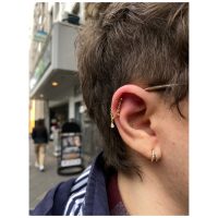 Goldener Piercing-Ring mit Kristallen am Ohr in urbaner Umgebung