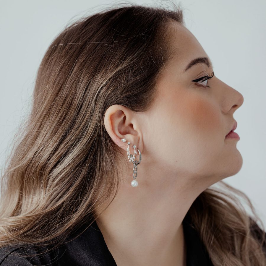 Frau mit silberner Piercingkette am Ohr, Haare zur Seite, helles Hintergrund