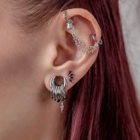 Ohr mit mehreren silbernen Piercings und einer Kette auf weißem Hintergrund