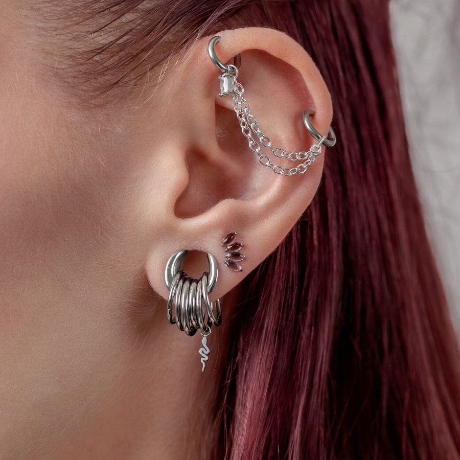 Ohr mit mehreren silbernen Piercings und einer Kette auf weißem Hintergrund