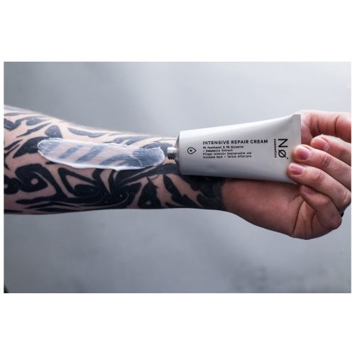 Hand hält No Cosmetics Intensiv Repair Cream, Arm mit Tattoo im Hintergrund