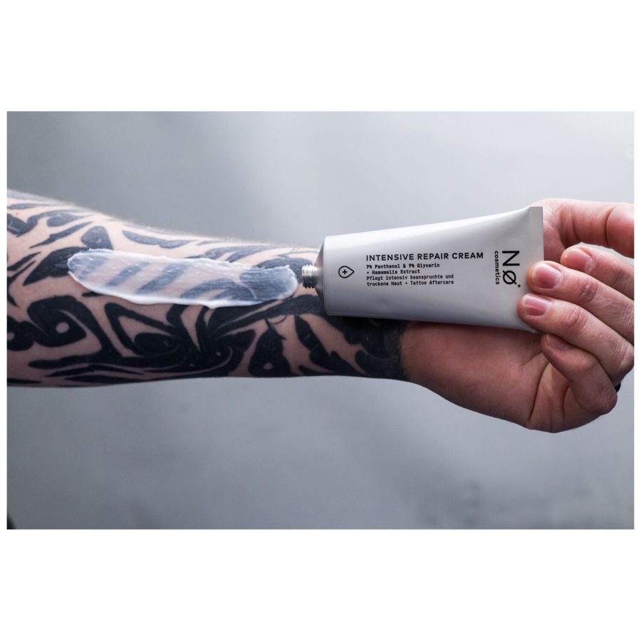 Hand hält No Cosmetics Intensiv Repair Cream, Arm mit Tattoo im Hintergrund