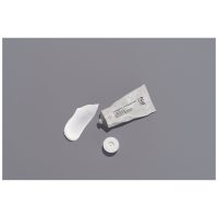 Graue Tube der Nø Cosmetics Intensiv Repair Cream mit abgenommenem Deckel und etwas Creme daneben auf grauem Hintergrund