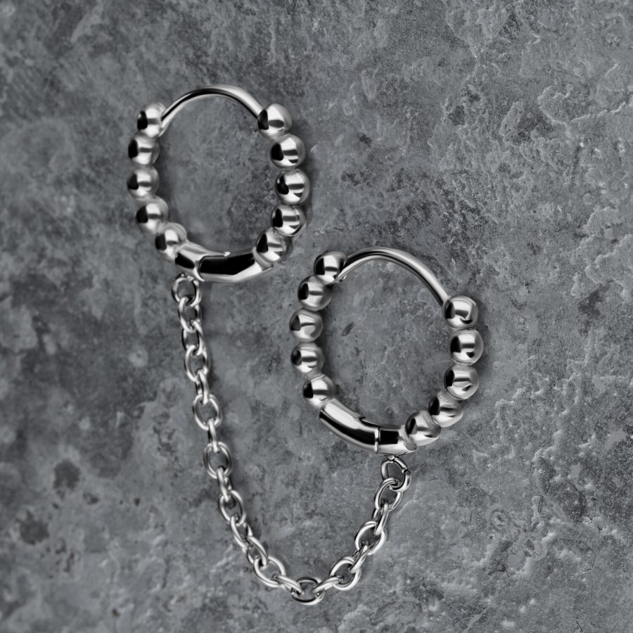 Silberne Doppel-Huggie-Ohrringe mit Kugeln und Kette auf grauem Hintergrund