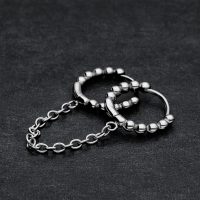 Zwei verbundene schwarze Huggie Piercingringe mit Kugeln auf dunklem Hintergrund