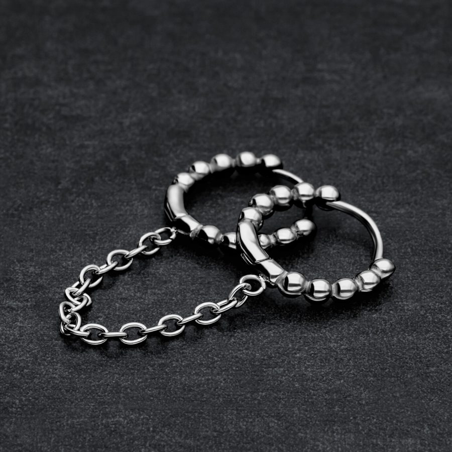 Zwei verbundene schwarze Huggie Piercingringe mit Kugeln auf dunklem Hintergrund