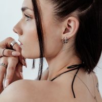 Nahaufnahme eines Ohrs mit schwarzen und silbernen Doppel Huggie Ball Hoops vor hellem Hintergrund