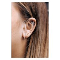 Goldenes Triangle Barbell Piercing am Ohr einer Person mit weiteren Piercings und Ohrtattoo