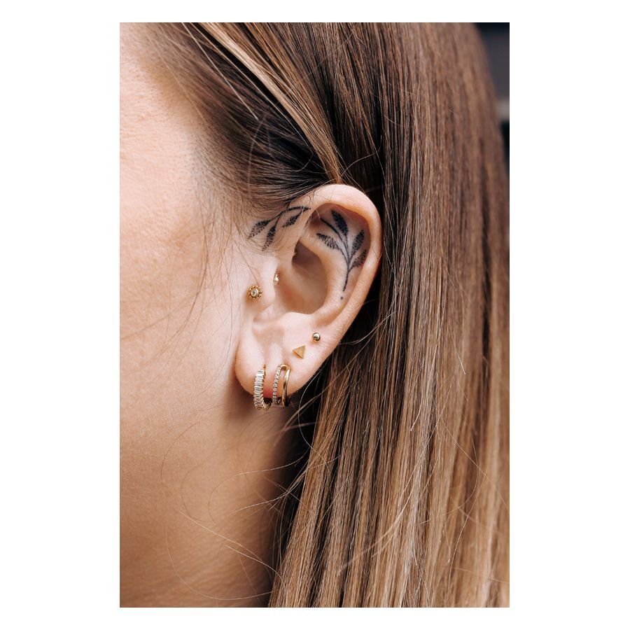 Goldenes Triangle Barbell Piercing am Ohr einer Person mit weiteren Piercings und Ohrtattoo