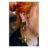 Goldener Clicker-Piercing im Ohr einer Person mit roten Haaren und Tätowierung