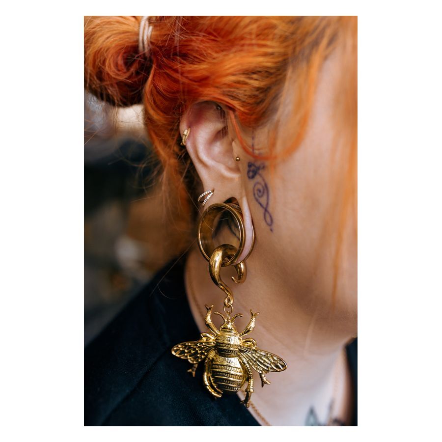 Goldener Clicker-Piercing im Ohr einer Person mit roten Haaren und Tätowierung