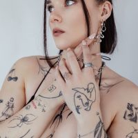 Person mit Schlangenring und Tattoos, trägt Schmuck auf weißem Hintergrund