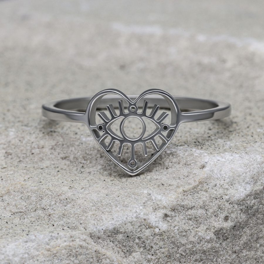 Silberner herzförmiger Ring mit Auge-Motiv auf grauem Stein