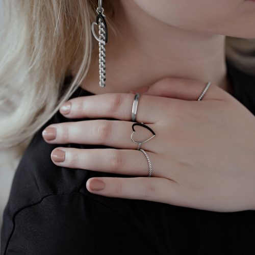 Nahaufnahme einer Hand mit zweifarbigem Herzring aus Chirurgenstahl, getragen neben anderen Ringen