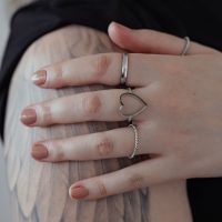 Silberner Herzring aus Chirurgenstahl an einer Hand auf tätowiertem Arm