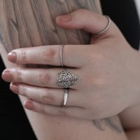 Silberner Blatt-Ring aus Chirurgenstahl auf einer tätowierten Hand vor hellem Hintergrund
