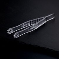 Zwei transparente, sterile Runde Piercingzangen liegen überkreuzt auf einem dunklen Hintergrund.