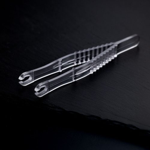 Zwei transparente, sterile Runde Piercingzangen liegen überkreuzt auf einem dunklen Hintergrund.