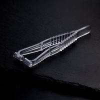 Transparente Septum Piercingzange aus Kunststoff auf dunklem, glattem Hintergrund