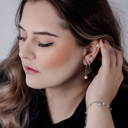 Frau mit Push Fit Pearl Peacock Aufsatz im Ohr, schwarzes Top, helle Haut
