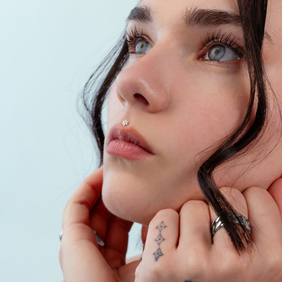 Nahaufnahme eines Gesichts mit silbernem Blumen-Piercing an der Nase, hellblauer Hintergrund