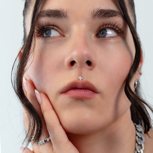Nahaufnahme eines Gesichts mit silbernem Blatt-Piercing an der Nase, Haare im Hintergrund