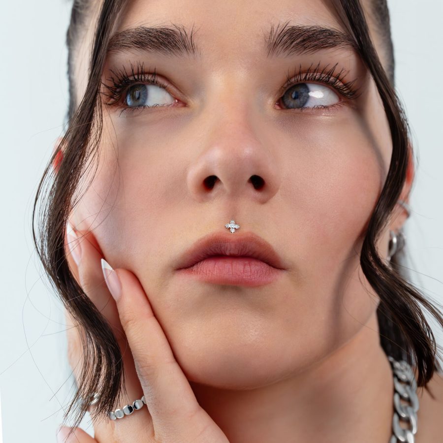 Nahaufnahme eines Gesichts mit silbernem Blatt-Piercing an der Nase, Haare im Hintergrund