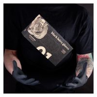 Person in schwarzem Shirt hält schwarze Piranha Latex-Handschuhe Schachtel vor dunklem Hintergrund