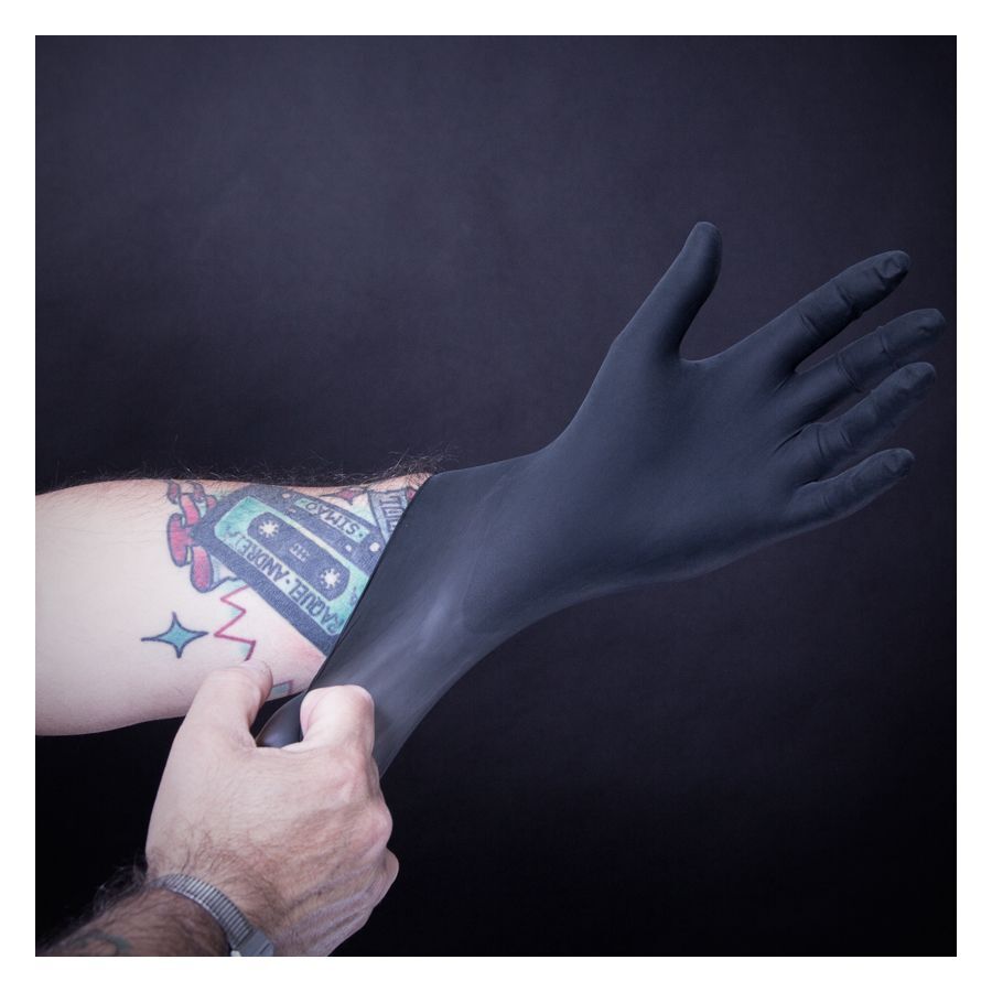 Schwarzer Latexhandschuh wird über tätowierten Arm gezogen