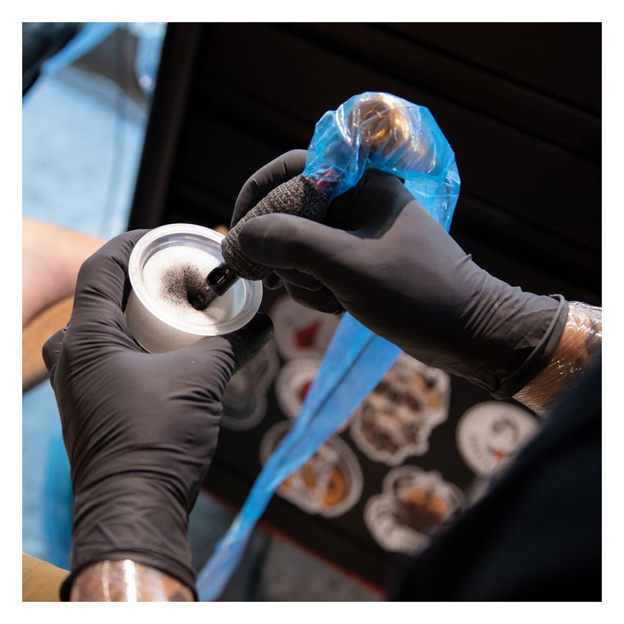 Schwarze Latexhandschuhe von Wildcat beim Tätowieren mit blauer Abdeckung
