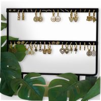 Schwarzes Ohrring-Display mit goldenen Ohrringen, umgeben von grünen Blättern