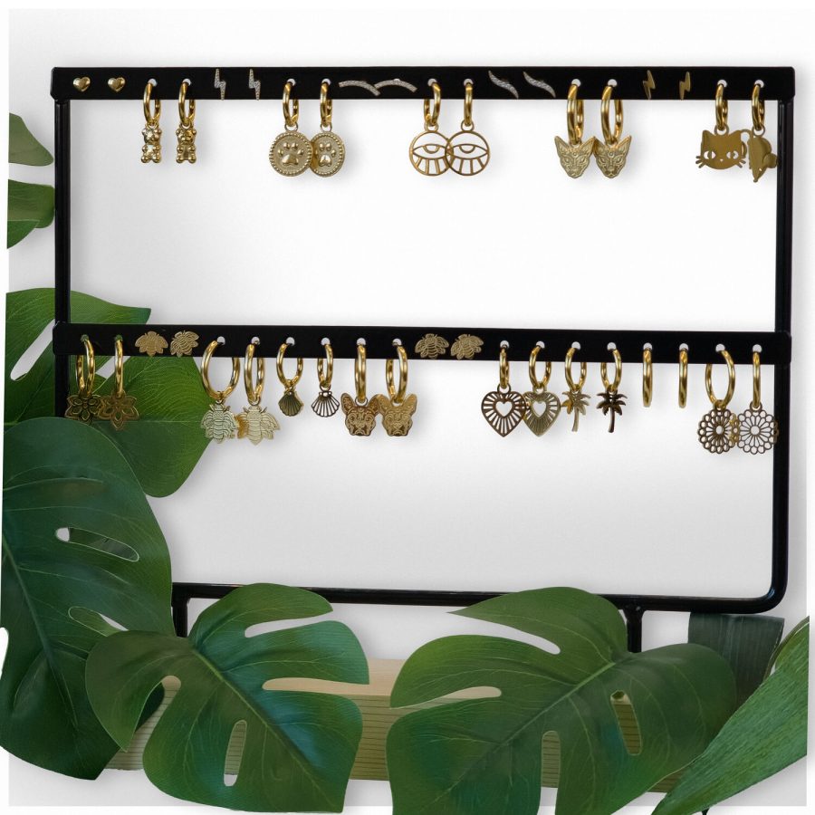 Schwarzes Ohrring-Display mit goldenen Ohrringen, umgeben von grünen Blättern