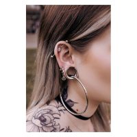 Silberne und schwarze Ear Saddles an einem Ohr mit Piercings, Tattoo im Hintergrund