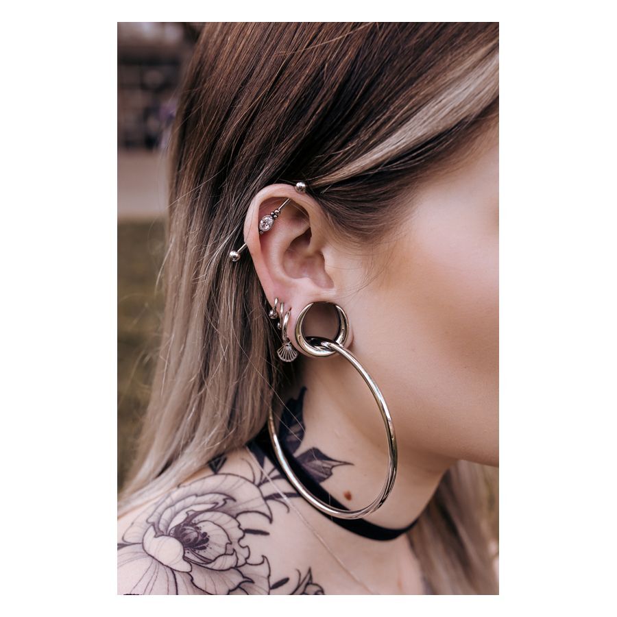 Silberne und schwarze Ear Saddles an einem Ohr mit Piercings, Tattoo im Hintergrund
