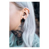 Nahaufnahme eines Ohrs mit schwarzen Monstera Ear Saddles und weiteren Piercings, im Hintergrund unscharf