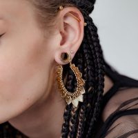 Nahaufnahme eines Ohrs mit geflochtenem Haar, das goldene Ear Saddles Maori trägt