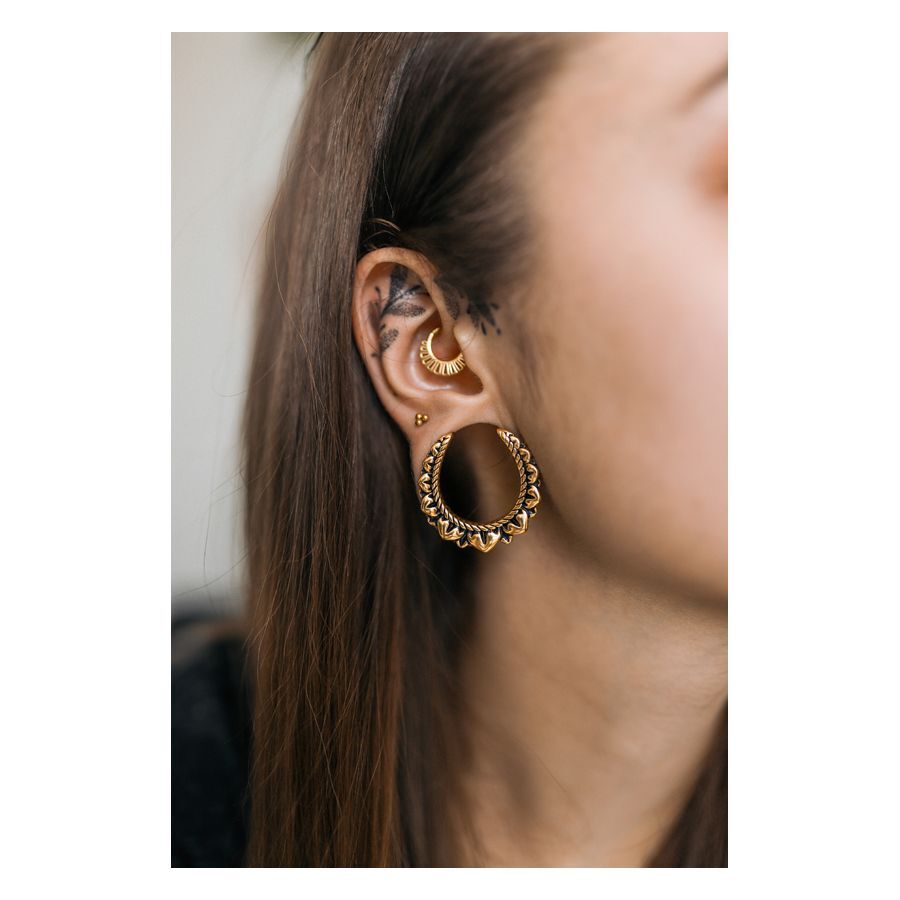 Goldene Blumen Ohrsättel in Ohr mit weiteren Piercings auf neutralem Hintergrund