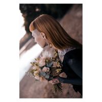 Person mit geflochtenen Ohrgewichten und Blumenstrauß am Seeufer