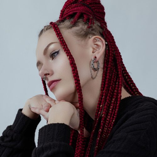 Frau mit roten Zöpfen trägt silberne Double Chain Ohrgewichte und schwarzen Pullover vor grauem Hintergrund