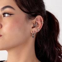 Nahaufnahme eines menschlichen Ohrs mit mehreren silbernen Piercings, darunter ein Sternanhänger, vor weißem Hintergrund.